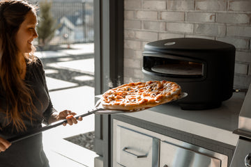 Person pulling a pizza out of a black oven in a kitchen.