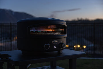 Black grill or smoker on a deck at dusk with mountains in the background.