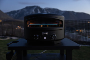 Black outdoor oven on a table with mountains in the background.